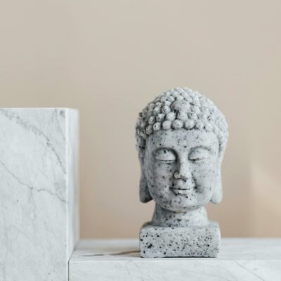 Granite statue of Buddha placed on white marble shelf against beige wall as religion symbol and home decoration element