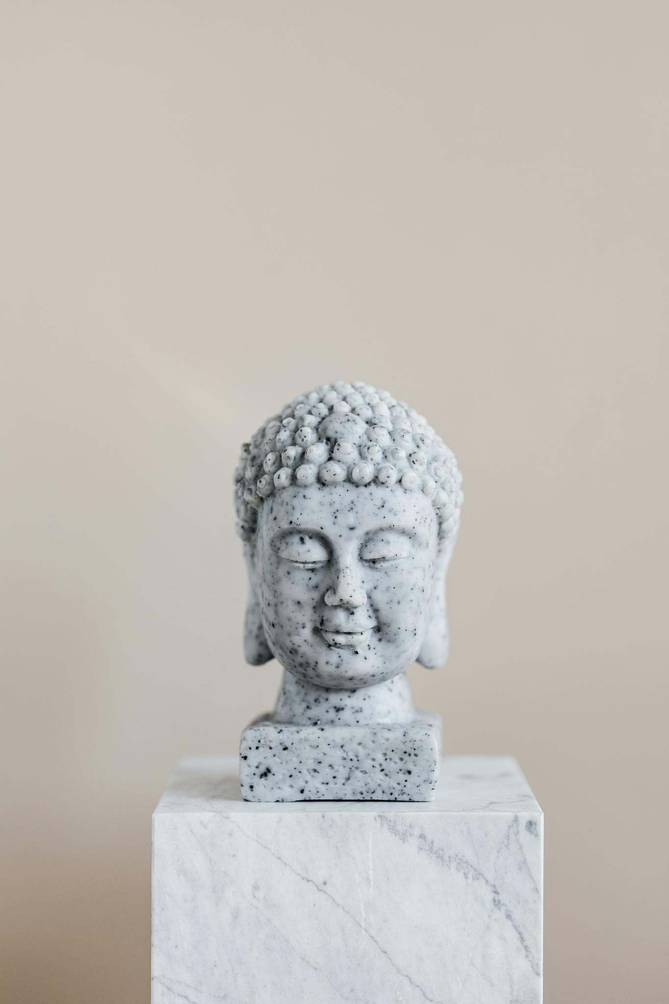 Stone bust of Buddha on marble stand